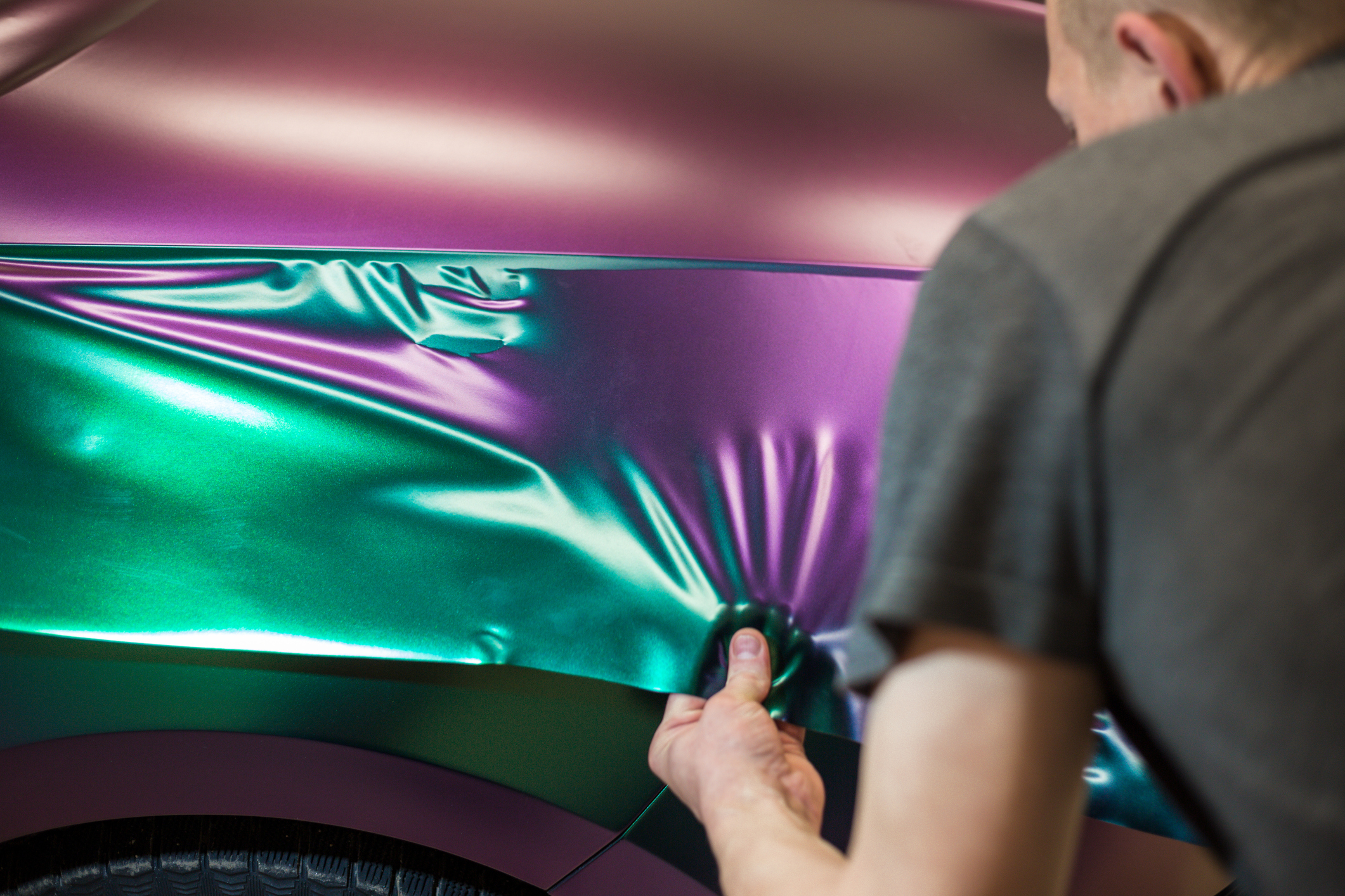 A specialist in wrapping a car with chameleon-colored vinyl film in the process of work. Car wrapping specialists cover the car with vinyl sheet or film. Selective focus.